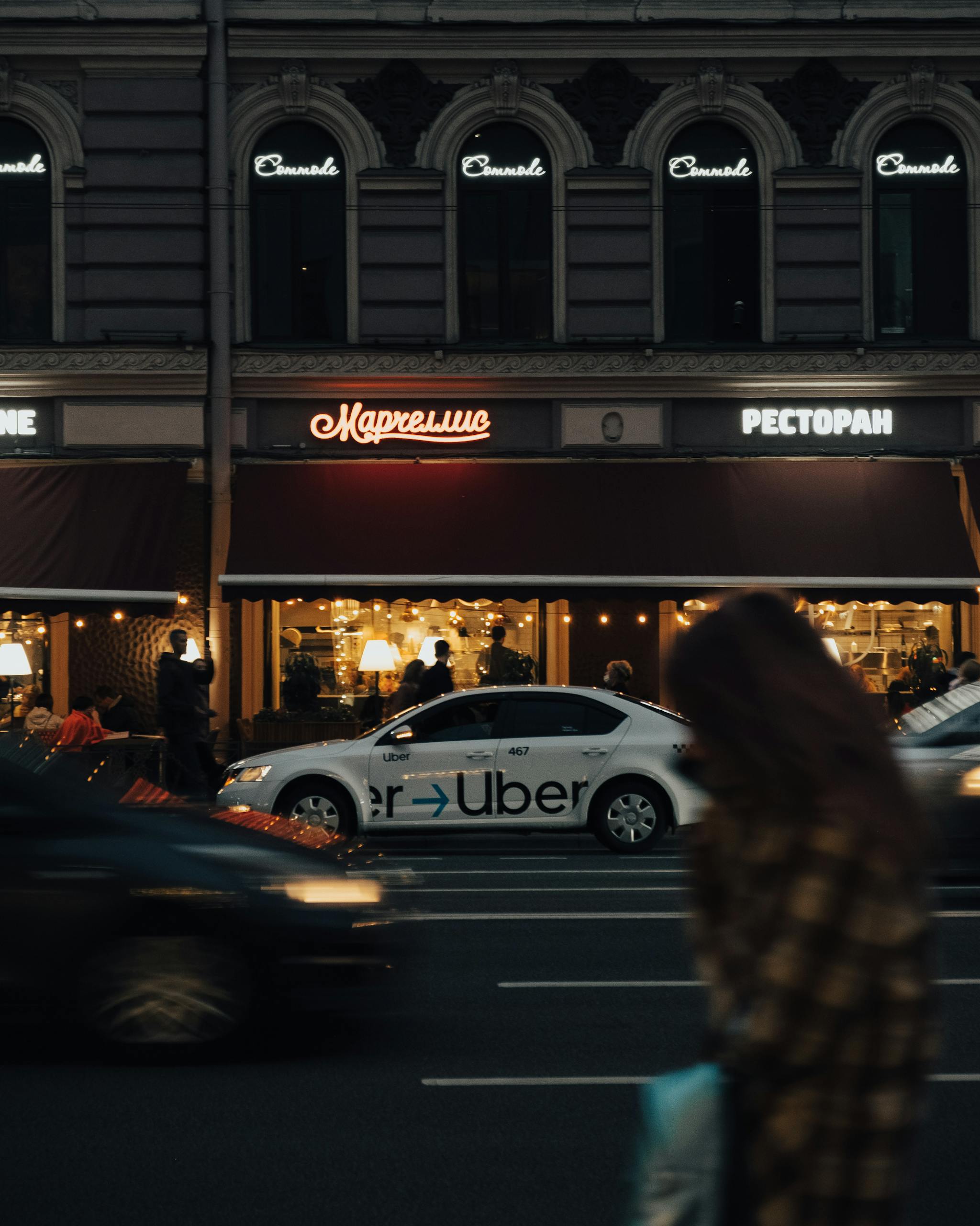 City evening scene with cars passing by a restaurant, showcasing urban nightlife.